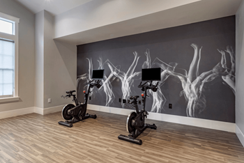 Two exercise bikes are placed in front of a wall mural